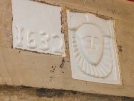 A stone wall with a white plaque showing the year 1632 and a carved face at Belmont Bridge in Henlle