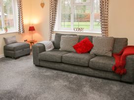 A gray sofa with cushions and a red throw next to a window with patterned curtains and a small side table with a lamp at Belmont Bridge in Henlle