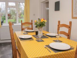 A dining table with yellow polka dot tablecloth set with plates glasses and cutlery with wooden chairs in a room with a window and yellow curtains at Belmont Bridge in Henlle