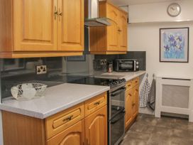 A kitchen with wooden cabinets a countertop a stove oven a microwave towels hanging on hooks a wall clock and a framed picture at Belmont Bridge in Henlle