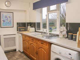 A kitchen with wooden cabinets a toaster a bread bin and a washing machine by a window with blue blinds at Belmont Bridge in Henlle