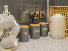 A kitchen counter with grey patterned mugs on a stand grey containers labeled tea sugar coffee and a cream electric kettle at Belmont Bridge in Henlle