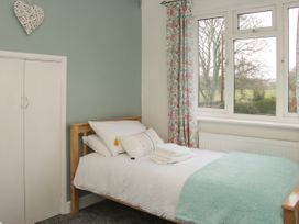 A bedroom with a single bed near a window with floral curtains at Belmont Bridge in Henlle