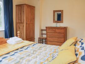 A bedroom with a bed with patterned bedding yellow pillows wooden wardrobe dresser and blue curtains at Belmont Bridge in Henlle
