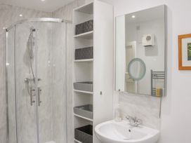 A bathroom with a glass shower enclosure a sink with a faucet and a mirror a white shelving unit with baskets and a wall-mounted vent at Belmont Bridge in Henlle