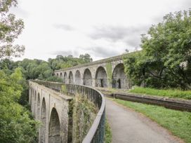 A stone aqueduct with multiple arches next to a river canal path surrounded by trees at Belmont Bridge in Henlle