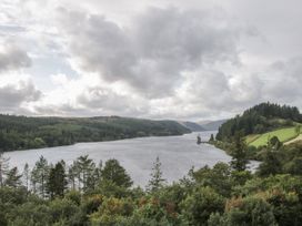 A lake surrounded by forested hills and a small tower on the shore at Belmont Bridge in Henlle