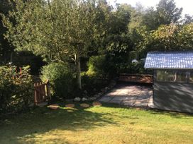 A garden with a lawn wooden steps a small wooden gate a tree a shed and a paved patio area at Belmont Bridge in Henlle