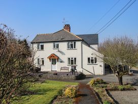 A two story house with white walls a gray roof and a garden with trees and bushes at Belmont Bridge in Henlle