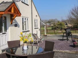 An outdoor patio area with a glass table and chairs a vase with yellow flowers a bench and a countryside view at Belmont Bridge in Henlle