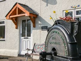 A white door with a wooden awning above it and a floral decorated bench outside at Belmont Bridge in Henlle