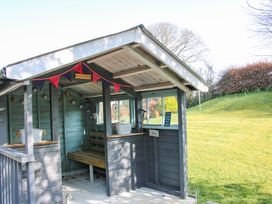 A small wooden garden shelter with a bench and bunting in a grassy outdoor area at Belmont Bridge in Henlle