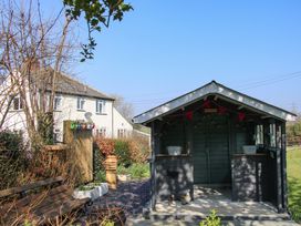 A garden with a wooden bench, a small shed with decorations, and a white house in the background at Belmont Bridge in Henlle