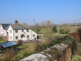 A two-story white house with a chimney and garden next to a field with trees and power lines at Belmont Bridge in Henlle