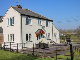 A two story house with multiple windows a small patio with table and chairs and a bench at Belmont Bridge in Henlle