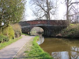A brick arch bridge over a canal with a walking path and trees at Belmont Bridge in Henlle