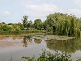 A lake with huts and trees at Willow Lodge At Bridge Lake Farm & Fishery Chacombe