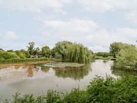 A lake with willow trees and fishing huts at Willow Lodge At Bridge Lake Farm & Fishery Chacombe
