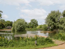 A pond with trees and a dock at Willow Lodge At Bridge Lake Farm & Fishery Chacombe