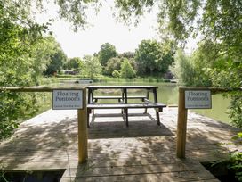 A wooden deck with a bench and signs by the water at Willow Lodge At Bridge Lake Farm & Fishery Chacombe
