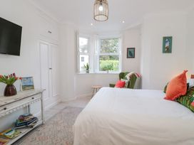 A bedroom with a bed and orange pillows a green armchair two plants on a window sill and a wooden console table with books at The Escape in Malvern