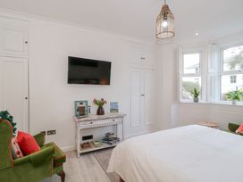A bedroom with a bed green armchairs a wall-mounted tv and white cabinets at The Escape in Malvern