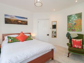 A bedroom with a wooden bed with white bedding and pillows a green armchair with cushions two paintings and a mirror on the wall at The Escape in Malvern