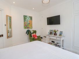 A bedroom with a green armchair a wall-mounted television and a console table with books and flowers at The Escape in Malvern