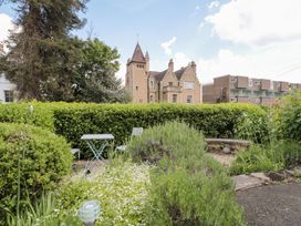 A garden with a metal table and chairs surrounded by bushes and flowers in front of a stone building at The Escape in Malvern