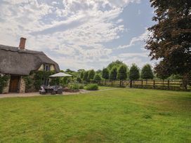 A thatched roof house with outdoor seating and trees at Garden View in Wellington