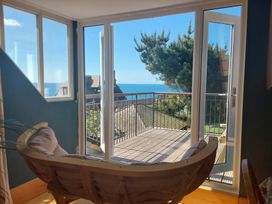 A room with a curved wooden chair facing glass doors leading to a balcony with a sea view at Sandy Combe in West Bay