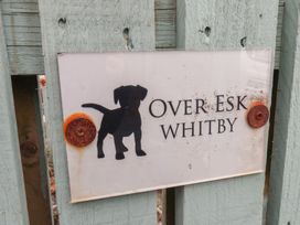 A sign with a silhouette of a dog and the text Over Esk Whitby mounted on a wooden fence