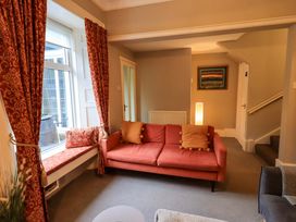A living room with a sofa, curtains, and painting at Yewbarrow Cottage in Grange-Over-Sands