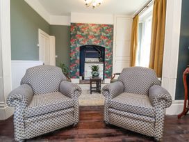 A seating area with two patterned armchairs a small table with a plant and a stove with floral wallpaper at The Woodlands in Berrynarbor