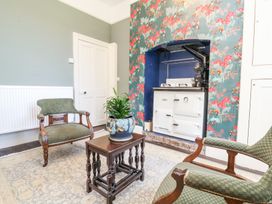 A room with two green upholstered chairs a wooden table with a plant and a stove set in a floral wallpapered alcove at The Woodlands in Berrynarbor