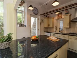 A kitchen with black countertop island with bread and bowl of vegetables near a door and cupboards at The Woodlands in Berrynarbor