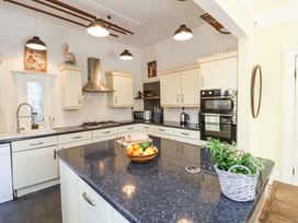 A kitchen with cream cabinets black countertops a built in oven a gas stove and a kitchen island with fruit and plants at The Woodlands in Berrynarbor