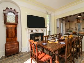A dining room with a wooden table set for breakfast near a fireplace and a tall wooden clock at The Woodlands in Berrynarbor