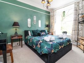 A bedroom with a double bed with patterned bedding two rolled towels on the bed two bedside tables with lamps a window with curtains and an open shelving unit at The Woodlands in Berrynarbor