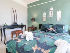 A bedroom with a bed featuring patterned bedding and pillows a bedside table with a lamp and a black desk with a brown stool at The Woodlands in Berrynarbor