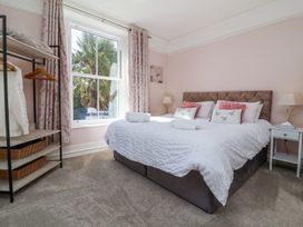 A bedroom with a large bed with white bedding and pink pillows next to a window with patterned curtains at The Woodlands in Berrynarbor