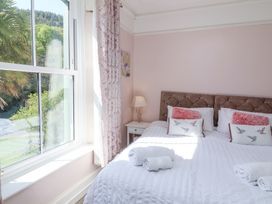 A bedroom with a bed set with white linens and pillows beside a window with patterned curtains and a nightstand lamp at The Woodlands in Berrynarbor