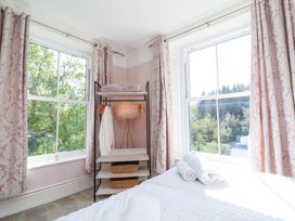 A bedroom corner with two windows pink patterned curtains a clothes rack with shelves and a bed with rolled towels at The Woodlands in Berrynarbor
