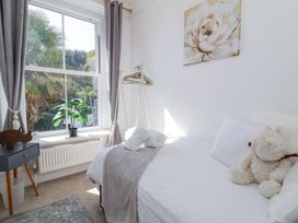 A bedroom with a bed that has white linens and a teddy bear a window with gray curtains and a plant on the windowsill a small table with a wooden decoration at The Woodlands in Berrynarbor