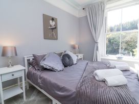 A bedroom with a bed made with gray pillows and blankets two white nightstands and lamps and a large window at The Woodlands in Berrynarbor