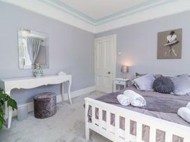 A bedroom with a white bed with pillows and towels a bedside table with a lamp a white dressing table with a mirror and a stool at The Woodlands in Berrynarbor