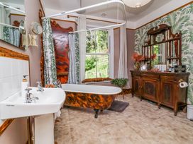 A bathroom with a freestanding bathtub sink wooden cabinet and a window with green foliage at The Woodlands in Berrynarbor