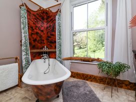 A bathroom with a freestanding bathtub a window with curtains a wooden alligator decoration a green plant on a stand and a towel rack at The Woodlands in Berrynarbor