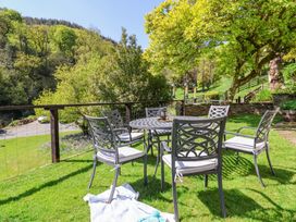 An outdoor seating area with a round metal table and six chairs with cushions on a grassy lawn near trees at The Woodlands in Berrynarbor
