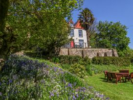 A garden with purple and white flowers and outdoor wooden furniture near a house with a red door at The Woodlands in Berrynarbor